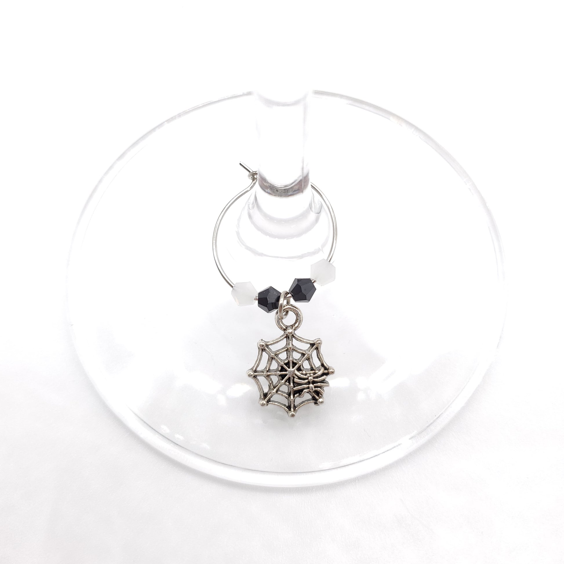 Spider web with a spider wine charm with white and black beads displayed on wine glass stem
