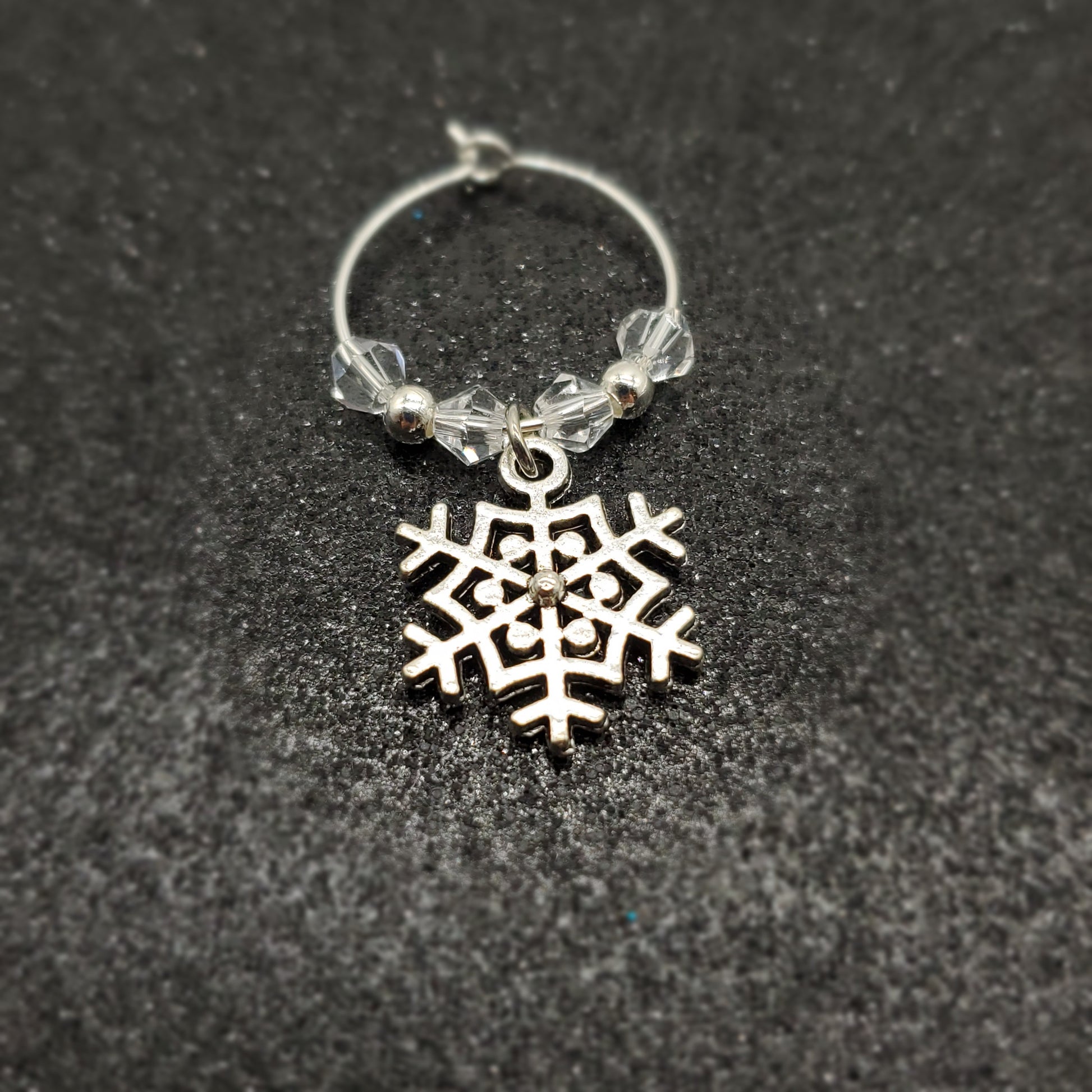 Silver snowflake  with clear beads wine glass charm on a black textured background