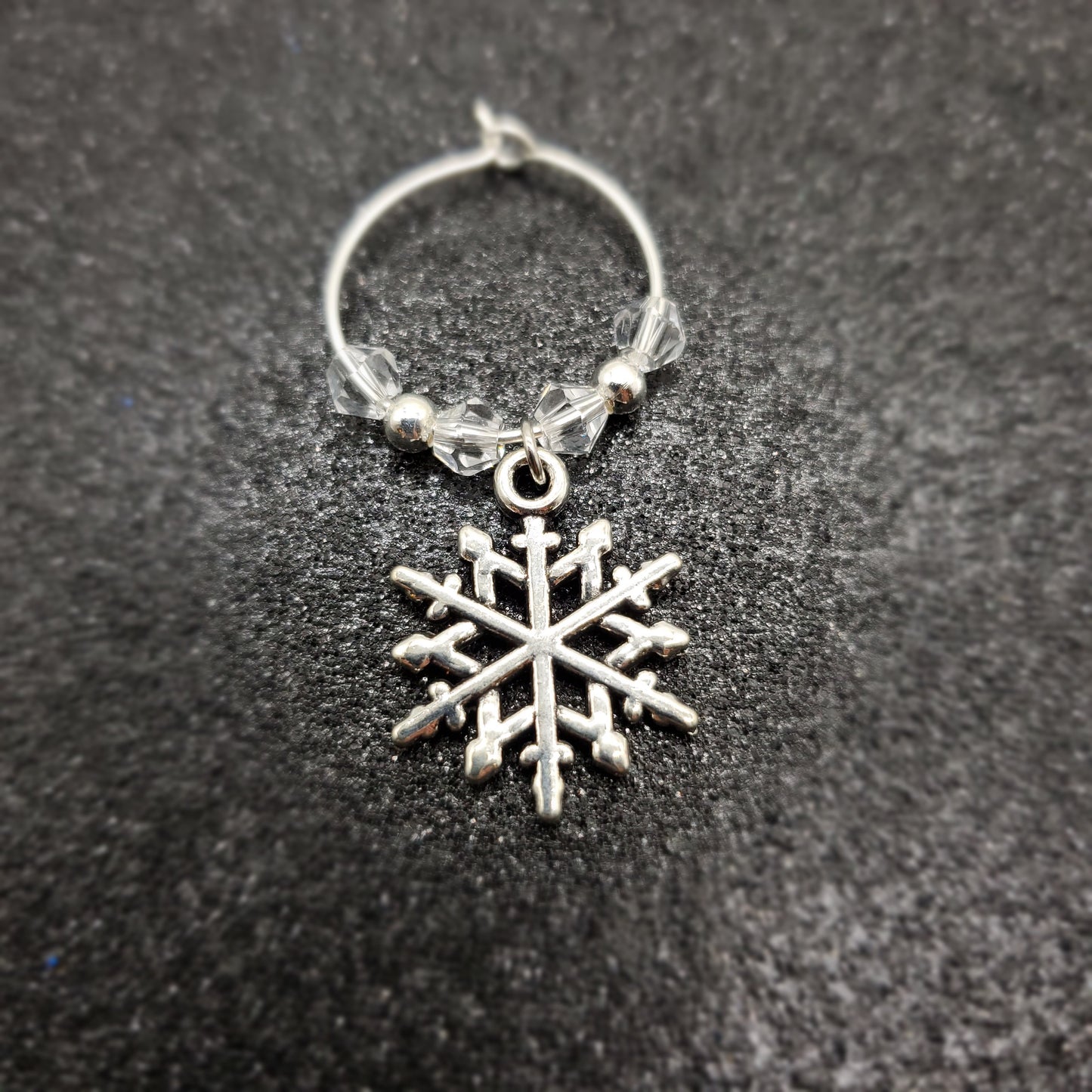 Silver hoop with a snowflake wine glass charm on a dark textured surface