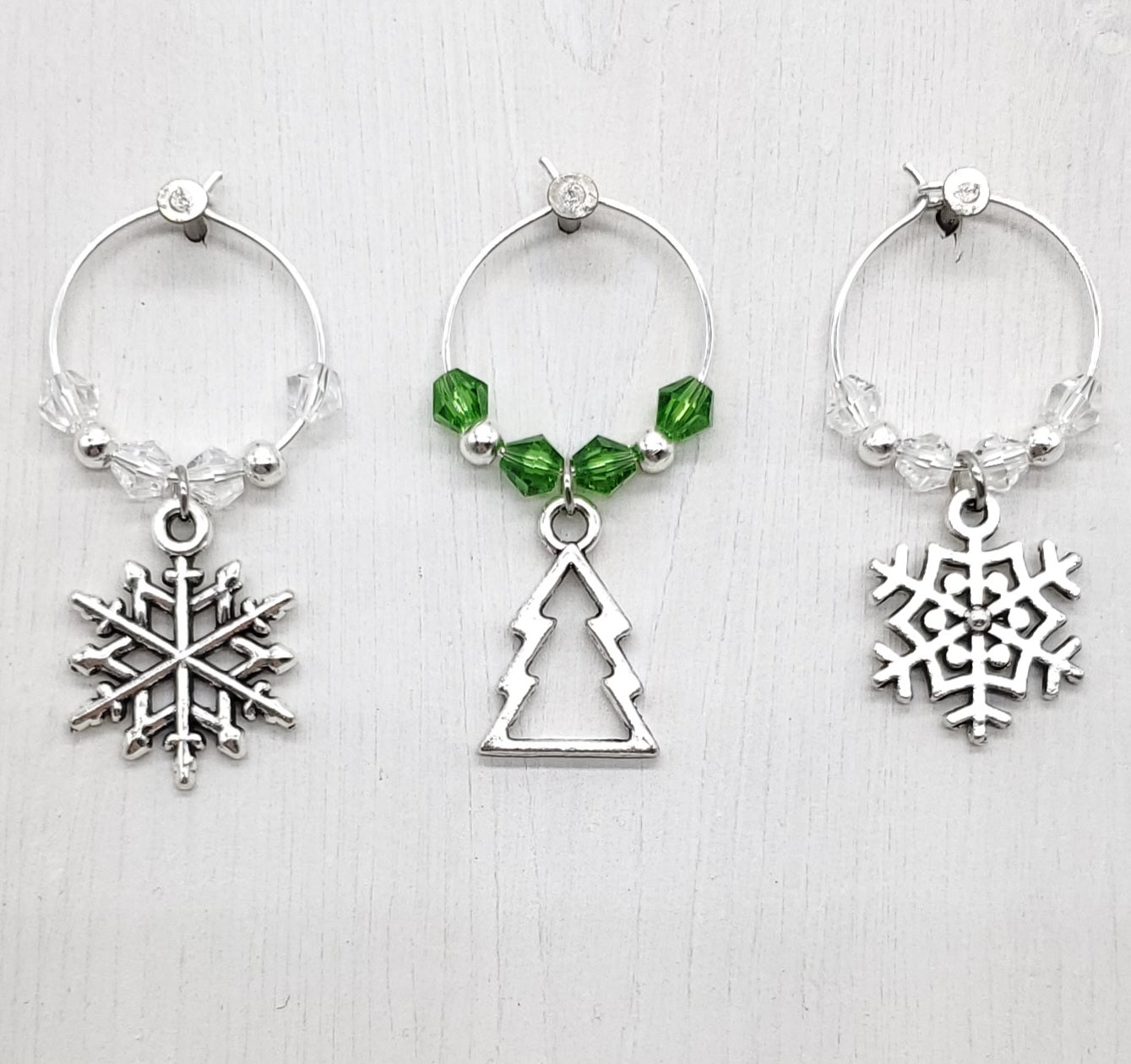 Three wine glass charms with snowflake, tree, and snowflake designs on a white background.